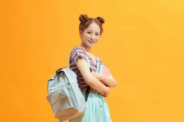 Stüdyo fotoğrafında sırt çantası ve kitaplar tutan genç bir öğrenci.