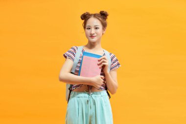 Asyalı bir kadın sırt çantasıyla ders kitapları tutuyor..