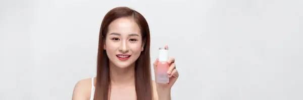 Uśmiechnięta Młoda Azjatycka Kobieta Pokazując Produkty Pielęgnacji Skóry Izolowane Tle — Zdjęcie stockowe