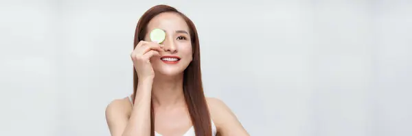 Young beautiful asian woman with cucumber slice on white background, panorama
