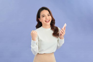 Mutlu, neşeli bir kadın ayakta durup cep telefonuna bakarken başarıyı kutluyor.