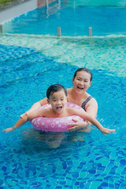 Mutlu Asyalı anne ve oğlu yüzme havuzunda poz veriyor.