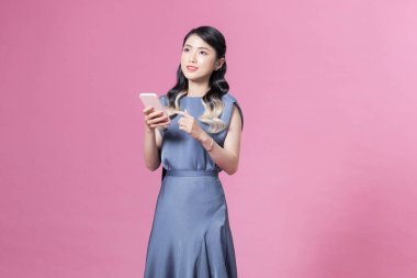 Güzel genç Asyalı kadın pembe üzerine izole edilmiş akıllı telefon kullanıyor.