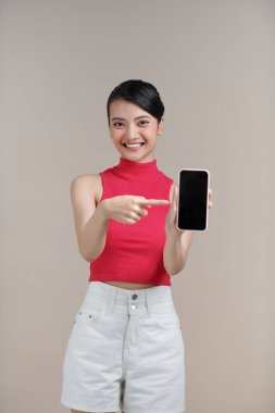 Gülümseyen kadın bej arka planda duran akıllı telefonu işaret ediyor..