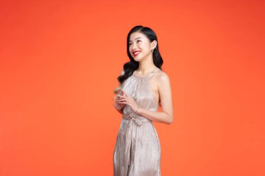 Kırmızı arka planda uzun, altın parti elbisesi giymiş bir kadın.