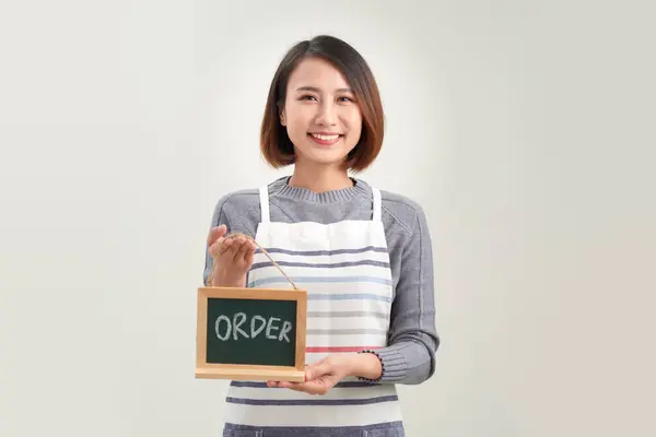 Young woman in apron holding board with order sign standing in white background