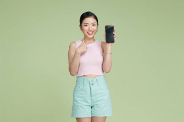 Gülümseyen kadın arka planda duran akıllı telefonu işaret ediyor.