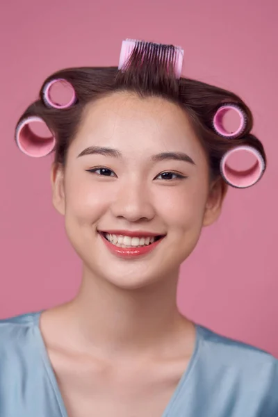 Beautiful young woman in hair rollers on pink background
