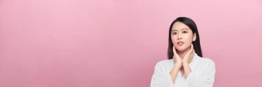 Gülümseyen güzel Asyalı kadın izole edilmiş stüdyo pembe arka planda yüzüne dokunuyor. Panorama