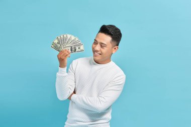 Elinde kağıt para olan yakışıklı Asyalı adam mavi arka planda tek başına duruyor.
