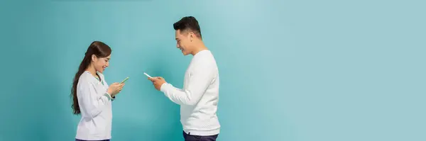 上网成瘾 两个年轻的恋人正忙着用蓝色横幅上的社交网络的手机 — 图库照片