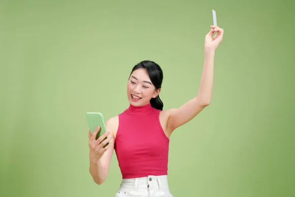 stock image Young Asian businesswoman  showing credit card and mobile phone isolated on green