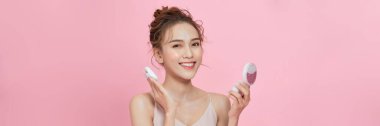  Young attractive lady applying cushion on her face with powder puff on pink background