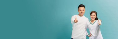 Charming positive husband wife cuddling showing you thumbs up isolated turquoise background