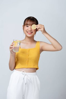 Güzel bir kadın elinde taze sarı bir limon ve ellerinde su olan bir bardak tutuyor.,