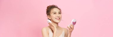 Portrait of beautiful girl smiling while applying face powder isolated over pink background