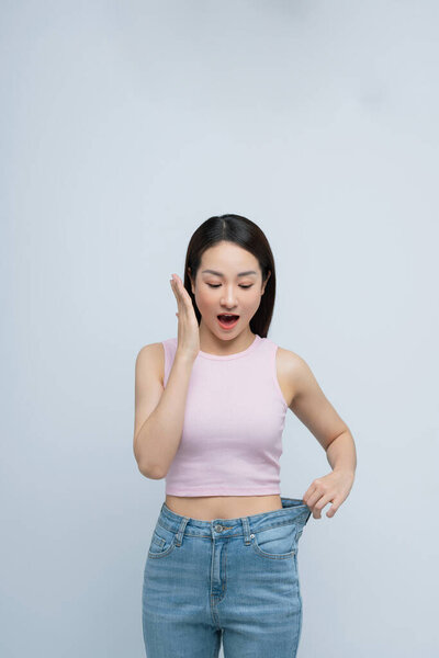 Successful weight loss, asian woman with too large jeans after effective diet, white background