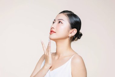 Güzel Asyalı kadın bej arka planda cildini gösteriyor..