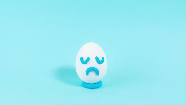 4K悲しい表情の卵が徐々に食べられる 悲観主義者の失われた人生の位置の概念 青の背景 動くなよ コピースペース — ストック動画