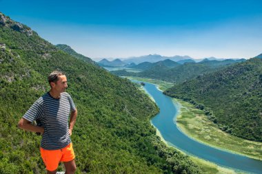 Pavlova Strana Manzara Noktası 'ndaki turist. Yeşil dağların, mavi gökyüzünün ve Skadar Gölü 'ne akan Crnojevica nehrinin güzel yaz manzarası. Karadağ. Seyahat kavramı.