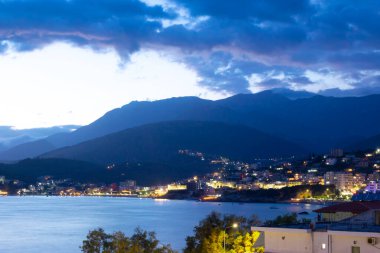 Twilight landscape of a resort Himare town located in a bay at the foot of the mountains. The village is beautifully lit by lanterns after sunset. Ionian sea. Albania.