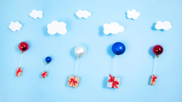 4k Gift boxes tied with red ribbons fly under the clouds on white, red, blue Christmas balls like balloons. Blue background. Greeting card. Stop motion animation. Copy space. Flat lay.