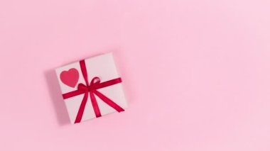 4k Red heart beats on pink gift box tied with a red ribbon. Greeting card for valentine's day. Pink background. Copy space. Flat lay. Looped stop motion animation.