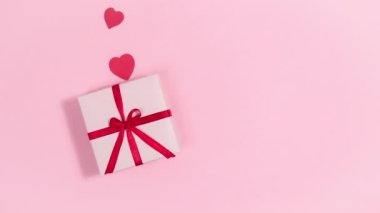 4k Red hearts, symbols of love, fly out of gift box tied with a red ribbon. Greeting card for valentine's day. Pink background. Copy space. Flat lay. Looped stop motion animation.