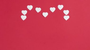 4k Small white hearts form a large heart shape with copy space in the center. Red background. Greeting card. Valentine's day. Flat lay. Stop motion animation.