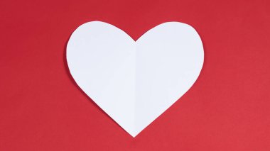 Big white heart on red background. Symbol of love. Greeting card. Concept of valentine's holiday, wedding and other occasions to express love. Copy space. Flat lay.