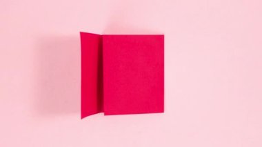 4k Red sheet of paper turns into three-dimensional origami heart. Pink background. Symbol of love. Greeting card. Concept of valentine's holiday, wedding and other occasions. Stop motion animation.