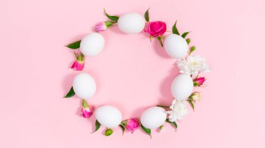 White eggs arranged in a circle are decorated with buds of natural flowers and green leaves. Pink background. Easter holiday. Greeting card. Template for design or text.
