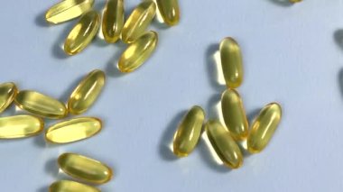 Yellow transparent capsules with liquid Omega 3 roll on a blue background. The concept of maintaining and improving health, Fish oil is an essential supplement for wellness. Slow motion. Close up.
