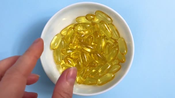 Woman Hand Takes Yellow Transparent Capsules Omega Blue Background Concept — Stockvideo