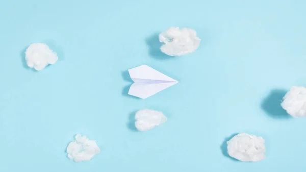 White paper airplane flies through white clouds on a blue background. Concept of travel, trips, air delivery. Flat lay. Copy space.