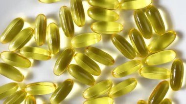 Beyaz zemin üzerinde sıvı Omega 3 olan sarı şeffaf kapsüller. Balık yağı sağlığın korunması ve iyileştirilmesi kavramı, refah için temel bir destektir. Ağır çekim. Kapat..