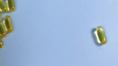 Yellow transparent capsules with liquid Omega 3 roll on a blue background. The concept of maintaining and improving health, Fish oil is an essential supplement for wellness. Slow motion. Close up.