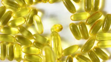 Yellow transparent capsules with liquid Omega 3 fall on a white background. The concept of maintaining and improving health, Fish oil is an essential supplement for wellness. Slow motion. Close up.