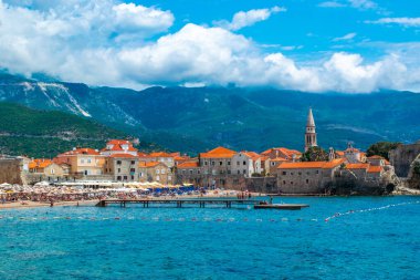 Kumlu Brijeg od Budva plajı ve eski şehir surları kalesi manzarası. Turuncu çatıları olan eski Budva kasabasının mimarisi. Güzel mavi yaz güneşli dağ manzarası. Karadağ.