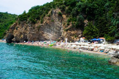 Budva yakınlarındaki kumlu Morgen plajında güneş pansiyonları ve şemsiyeler. Yaz güneşli manzarası. Karadağ.