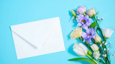 Mavi arka planda doğal çiçekler belirir ve buket oluştururlar. Yanında beyaz bir zarf var. Doğum günü kartı, anne, kadınlar günü ya da başka bir etkinlik için tebrik kartı. Boşluğu kopyala.