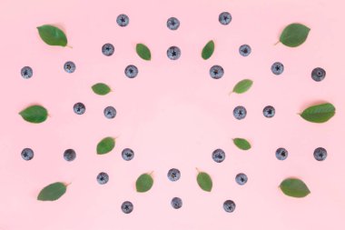 Olgun yaban mersini ve yeşil yapraklar pembe arka planda daire şeklinde dizilmiş. Böğürtlen mevsimi ve düzgün beslenme kavramı. Boşluğu kopyala.