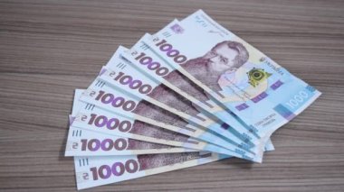 Kadınların elleri masaya serilmiş bin tane Hryvnia Ukrayna banknotunu alıyor. Gelir, iş ve kazanç kavramı.