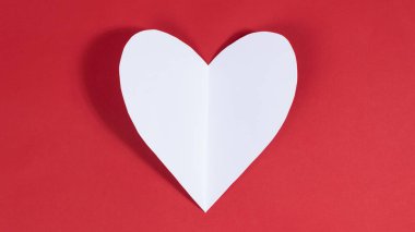 Big white heart on red background. Symbol of love. Greeting card. Concept of valentine's holiday, wedding and other occasions to express love. Copy space. Flat lay.