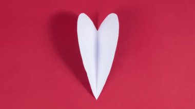 4k Büyük beyaz kalp kanatlarını çırpıyor. Aşkın sembolü. Tebrik kartı. Sevgililer Günü tatili, düğün ve aşkı ifade etmek için diğer fırsatlar kavramı. Kırmızı arka plan. Hareket animasyonunu durdur. Düz yatıyordu.