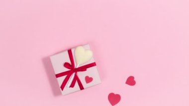 4k Pembe hediye kutusunun yanında kırmızı kurdele ve beyaz çikolata kalp şekeri, kalpler uçup gidiyor, aşkın sembolleri. Sevgililer Günü için tebrik kartı. Pembe arka plan. Uzayı kopyala Düz yatıyordu. Hareketi durdur
