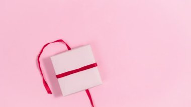 Kırmızı kurdeleli 4K hediye kutusu ve kalp şeklinde beyaz çikolata şekeri. Yürekler uçar gider, aşkın sembolleri. Sevgililer Günü tebrik kartı. Pembe arka plan. Uzayı kopyala Hareketi durdur.