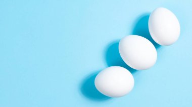 Mavi arka planda üç beyaz tavuk yumurtası. Minimum konsept. Paskalya ya da protein yiyeceği kavramı. Yakın plan. Boşluğu kopyala.