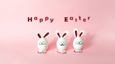Mutlu Paskalyalar. Açık pembe renkli arka planda izole edilmiş beyaz tavuk yumurtasından yapılmış üç sevimli tavşan. Tatil tebrik kartı. Boşluğu kopyala.