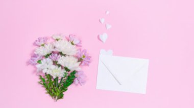 Bir buket doğal kasımpatı çiçeğinin yanında kalplerin uçup gittiği beyaz bir zarf bulunur. Anneler günü için tebrik kartı, kadınlar günü, doğum günü ya da başka bir şey. Pembe arkaplan. 